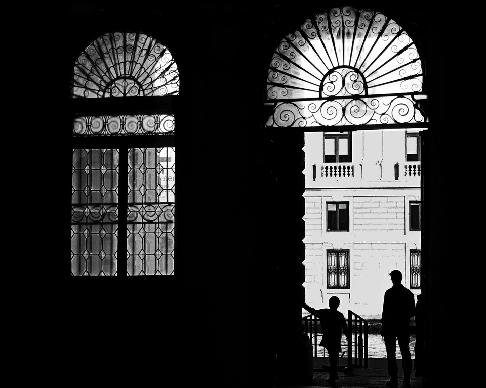 A silouette of two people standing in a large brick doorway with ornamental ironworks in the windows