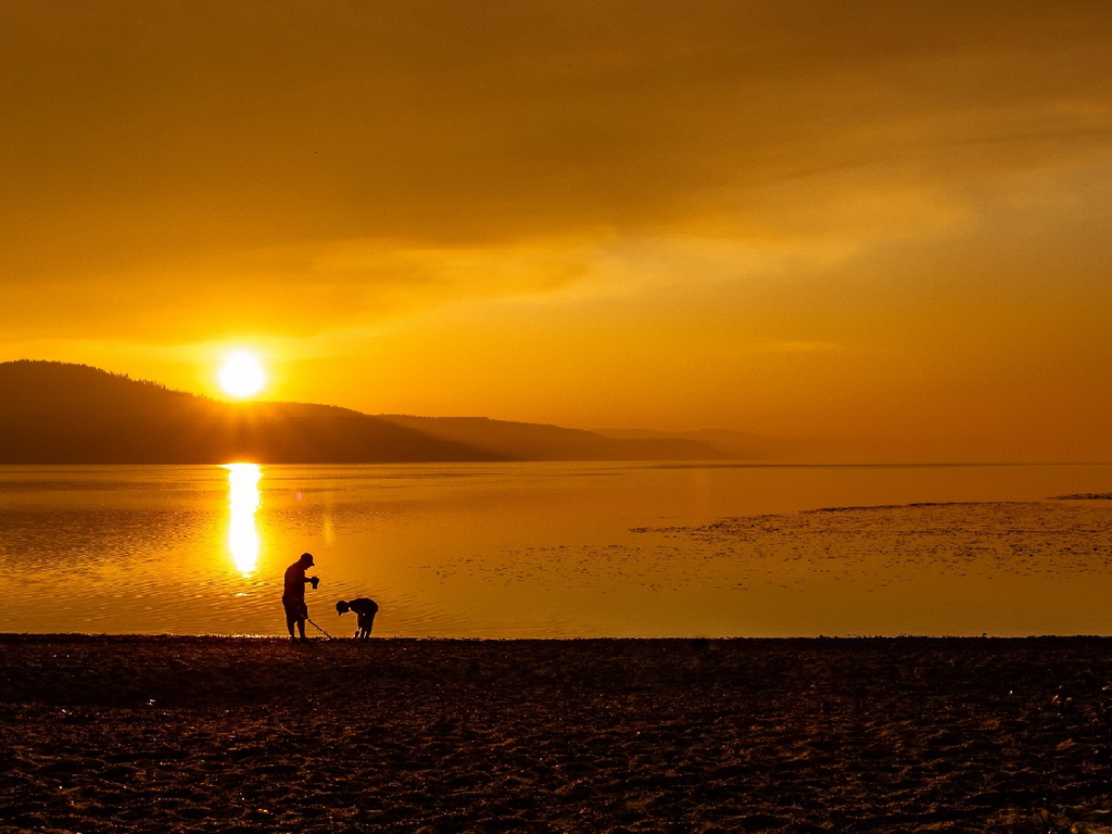Two people using metal detector and digging in sand on a beach during sunset